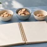 Blank notebook beside three bowls of wooden counters and a small cream house model.